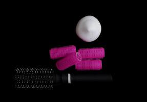 Different products for hair styling - comb, curlers and volume styling mousse isolated on black background with copy space photo