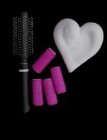 Different products for hair styling - comb, curlers and volume styling mousse isolated on black background with copy space photo