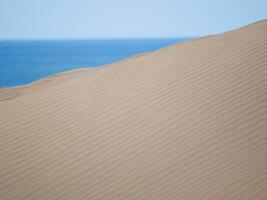 Sand textured pattern with copy space close up in Maspalomas, Gran Canaria. Abstract background wallpaper. Sand waves in a desert dune at the background of the sea photo