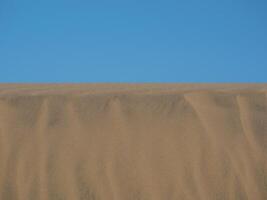 Sand textured pattern with copy space close up in Maspalomas, Gran Canaria. Abstract background wallpaper. Sand waves in a desert dune against the sky photo