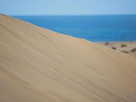 Sand textured pattern with copy space close up in Maspalomas, Gran Canaria. Abstract background wallpaper. Sand waves in a desert dune at the background of the sea photo