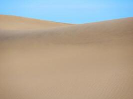 Sand textured pattern with copy space close up in Maspalomas, Gran Canaria. Abstract background wallpaper. Sand waves in a desert dune against the sky photo