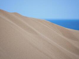 Sand textured pattern with copy space close up in Maspalomas, Gran Canaria. Abstract background wallpaper. Sand waves in a desert dune at the background of the sea photo