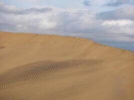 Sand textured pattern with copy space close up in Maspalomas, Gran Canaria. Abstract background wallpaper. Sand waves in a desert dune against the sky photo