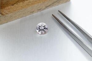macro mineral faceted stone Morganite with tweezers on a gray background photo