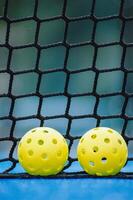 two pickleball balls on a blue pickleball court, with the net in the background photo