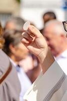 a catholic priest holding a host during the sacrament of communion at an exterior service photo