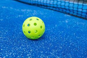 pickleball ball on a blue pickleball court, with the net in the background photo
