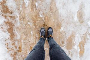 Legs in denim jeans encased in grey shoes stand on snowcovered ground photo