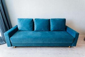 Electric blue studio couch with pillows in a living room next to a window photo