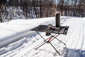 Folding Compact Camping Camping Table, Camping Utensils Stand Against Snow Background. photo