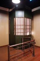 A prison cell made of green wood with a fenced building around it photo