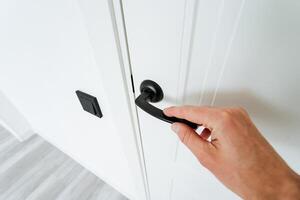 Hand gesturing to open a white door with a black handle photo
