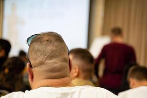 A man in sunglasses sits in a classroom watching a presentation photo