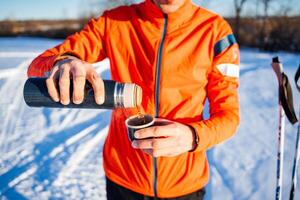 a man in an orange jacket is pouring a cup of coffee from a thermos photo