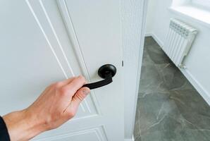 With a swift gesture, the person opens the white door with a black handle photo