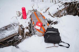 First aid kit is on the backpack next to a pink thermos with tea, walking alone in the winter forest, trekking photo