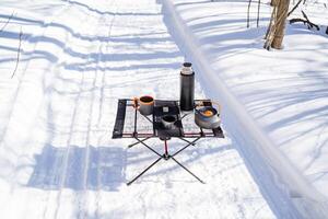 A view from above on the dishes on the hike that are on the table, a folding tourist table, a thermos and a kettle, aluminum dishes. photo
