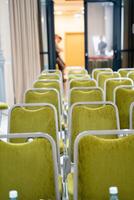 A conference room has rows of green chairs with water bottles photo