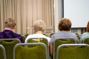 People sit in green chairs in front of a projector screen photo