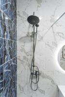 A shower head hangs on a bathroom wall next to a mirror photo