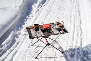 Camping utensils standing on the table in the forest, red first aid kit, folding camping table. photo