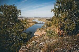 River flowing in valley with trees and rocks, under open sky photo