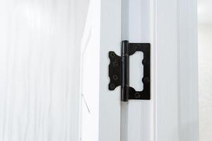A closeup view displaying a black door hinge affixed on a white door photo