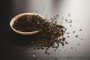 Liquid tea in a bowl sits beside a stack of tea leaves on a table photo