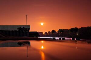 A sunset casts vibrant colors over water, with a stunning building photo
