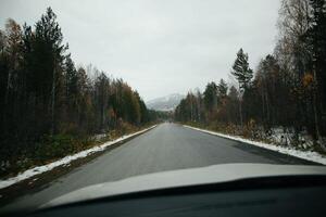 A vehicle drives on an asphalt road through snowy woods photo
