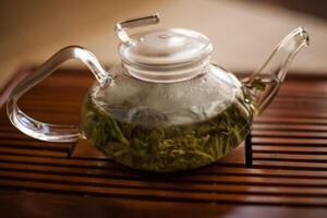 a glass teapot filled with green tea is sitting on a wooden table photo