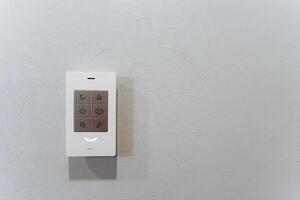 An electronic device, resembling a rectangular gadget, hanging on the wall with a white remote control. photo