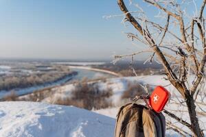 Winter landscape on mountain peak, red first aid kit on a hike, trekking in winter in the mountains, camping in the forest, survival alone in nature. photo