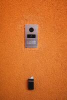 Modern door intercom system with camera isolated on orange wall background photo