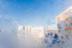 Frozen snowflakes on the window, frost drawing its patterns on the glass, cold season, winter outside the window. photo