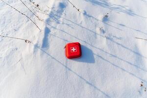 On the snow there is a first-aid kit, a conceptual photo of medical aid on a hike, a red box with medicines.