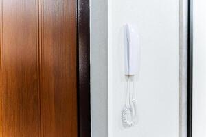 A white intercom hangs on the wall near the front door of the house. Telephone handset with wire, call the hotel administrator by phone. photo
