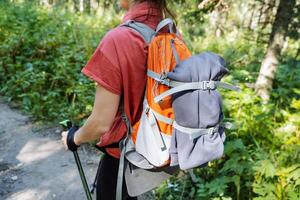 View from the back of a tourist backpack with things, equipment for hiking, straps on a backpack, a girl walking in the forest with poles, trekking. photo