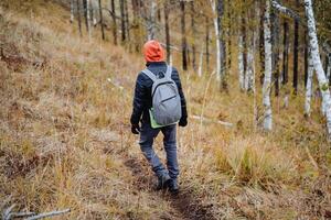 A man with a backpack on his back confidently walks along a mountain trail, a hiker on a hike moves along the azimuth, autumn hiking in a national park. photo