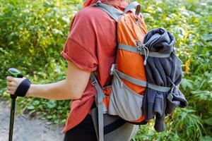 Man with backpack for things on a hike, girl tourist walking in the mountains, trekking with a backpack, a jacket fastened to a bag, a hand with a trekking pole. photo