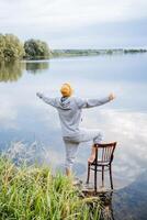 The guy is standing with his back to the camera, stretching his arms to the sides, enjoying the view of the lake, a man relaxing in nature, delight and happiness, fresh air. photo