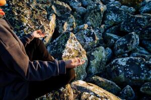 Meditation in nature in the mountains, calming the mind, taking care of the body, zen practice, yoga in the morning sitting in the lotus position, side view, hands folded on knees. photo