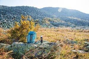 tourist equipment, a backpack for a hike stands on a stone, mountain tourism, a thermos with tea stands on a stone, a sunny day, autumn in the mountains. photo