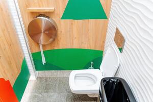 Internal toilet cubicle, white toilet bowl hanging, toilet paper in a metal case, men's room in a shopping center. photo