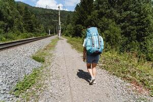 Hiker on a hike with a large backpack, women's legs rear view, summer vacation in the mountains in nature, tourist walk, big bag, trekking on the road in the forest photo