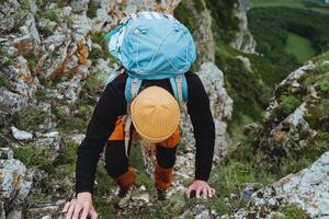 A tourist guy climbs up the rocks, a man climbs with a backpack uphill, a climber clings to stones with his hands, a dangerous ascent into the mountains. photo
