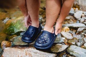 The child's feet are shod in slate, the boy wears shoes for swimming in the sea, protection of the feet from cuts, slaps for swimming, the boy stands on the bank of a stone river photo
