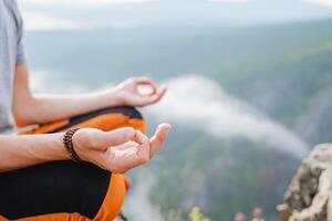 Hands fingers folded in mudra yogic practice, the guy meditates sitting in the mountains against the background of clouds, the silence of the inner world. photo