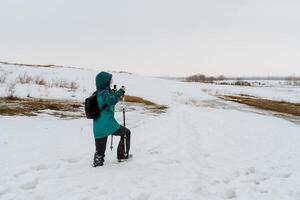 A person walks in the snow with sticks, Nordic walking in winter, winter hiking in cold weather, a tourist travels through the forest. photo